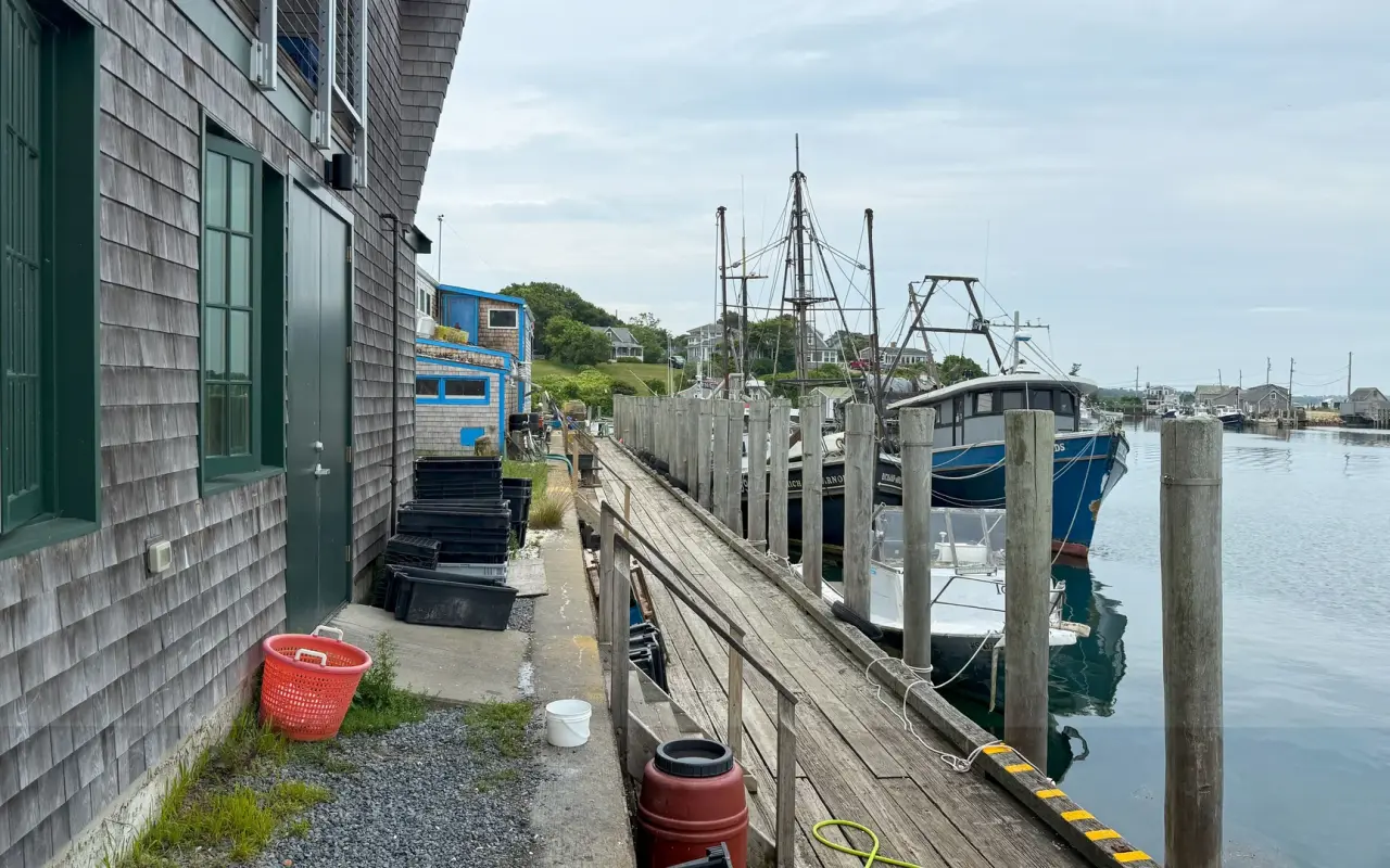 Fish totes and a red basket on Dutcher Dock in Menemsha with fishing boats moored alongside