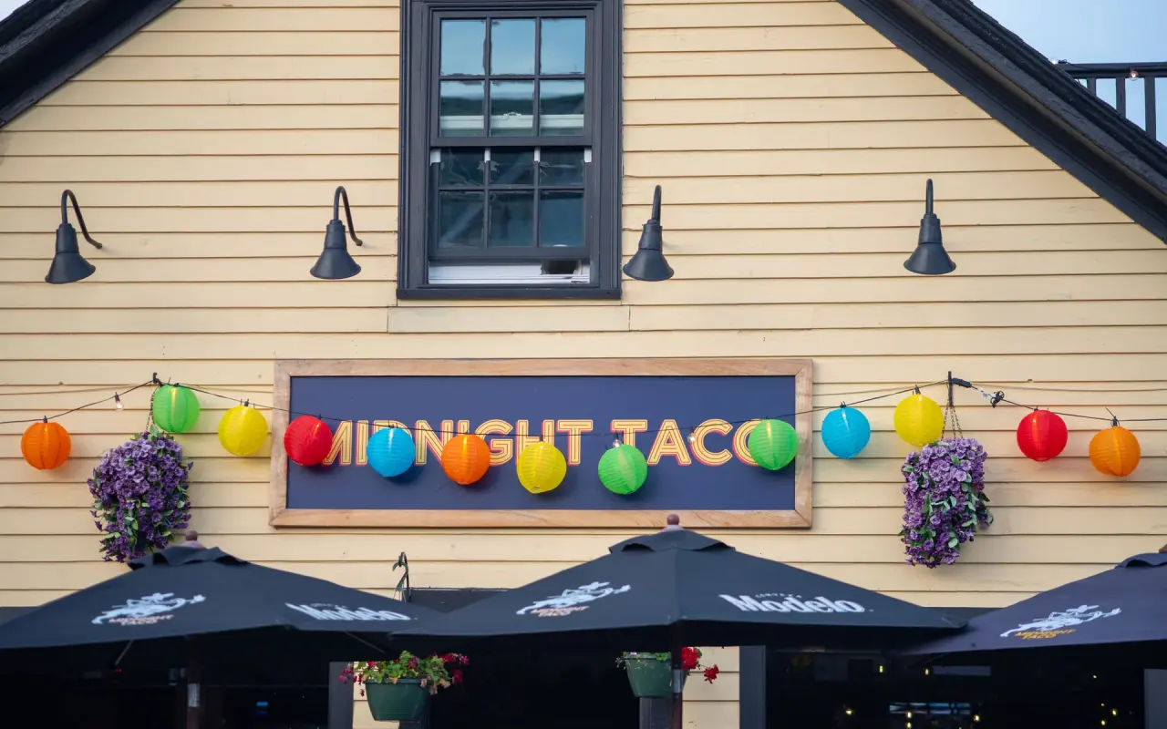 Colorful paper lanterns hanging over the Midnight Taco sign on a yellow building