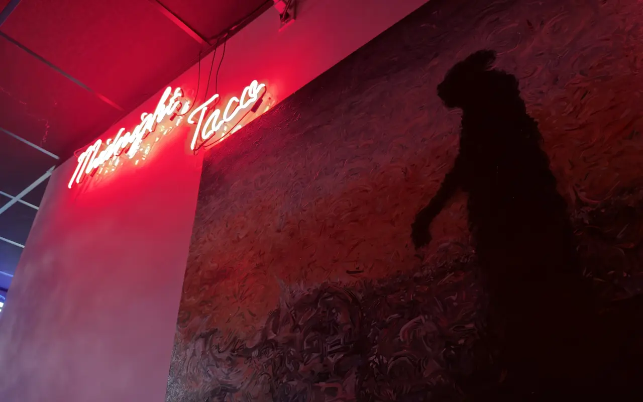 The red neon Midnight Taco sign above a dark painted mural of a figure, inside Midnight Taco in Oak Bluffs
