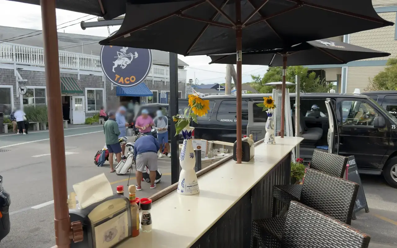 Outdoor bar counter under black umbrellas at Midnight Taco with black taxi vans parked behind it