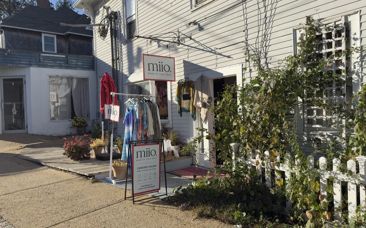 White clapboard shop front of Miio, Made in Italy Only, on Main Street in Vineyard Haven, with a sandwich board, a rack of dresses and scarves hanging by the door