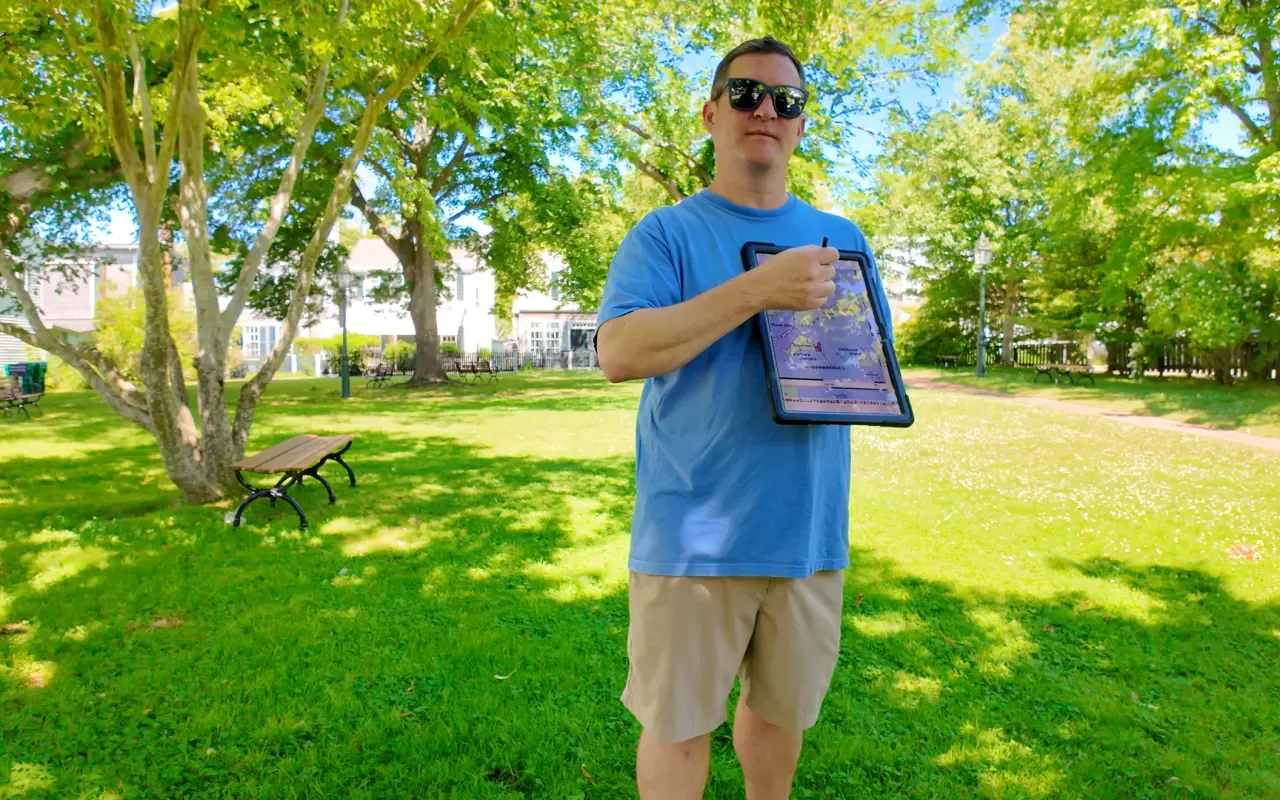 Mike Currid holding up a tour tablet in an Edgartown park