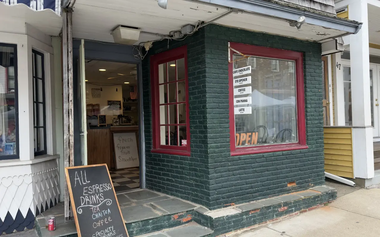 The green painted brick entrance of Mister Pugg's Mugg coffee shop in Oak Bluffs with a chalkboard listing espresso drinks and a fresh frozen fruit smoothies sign