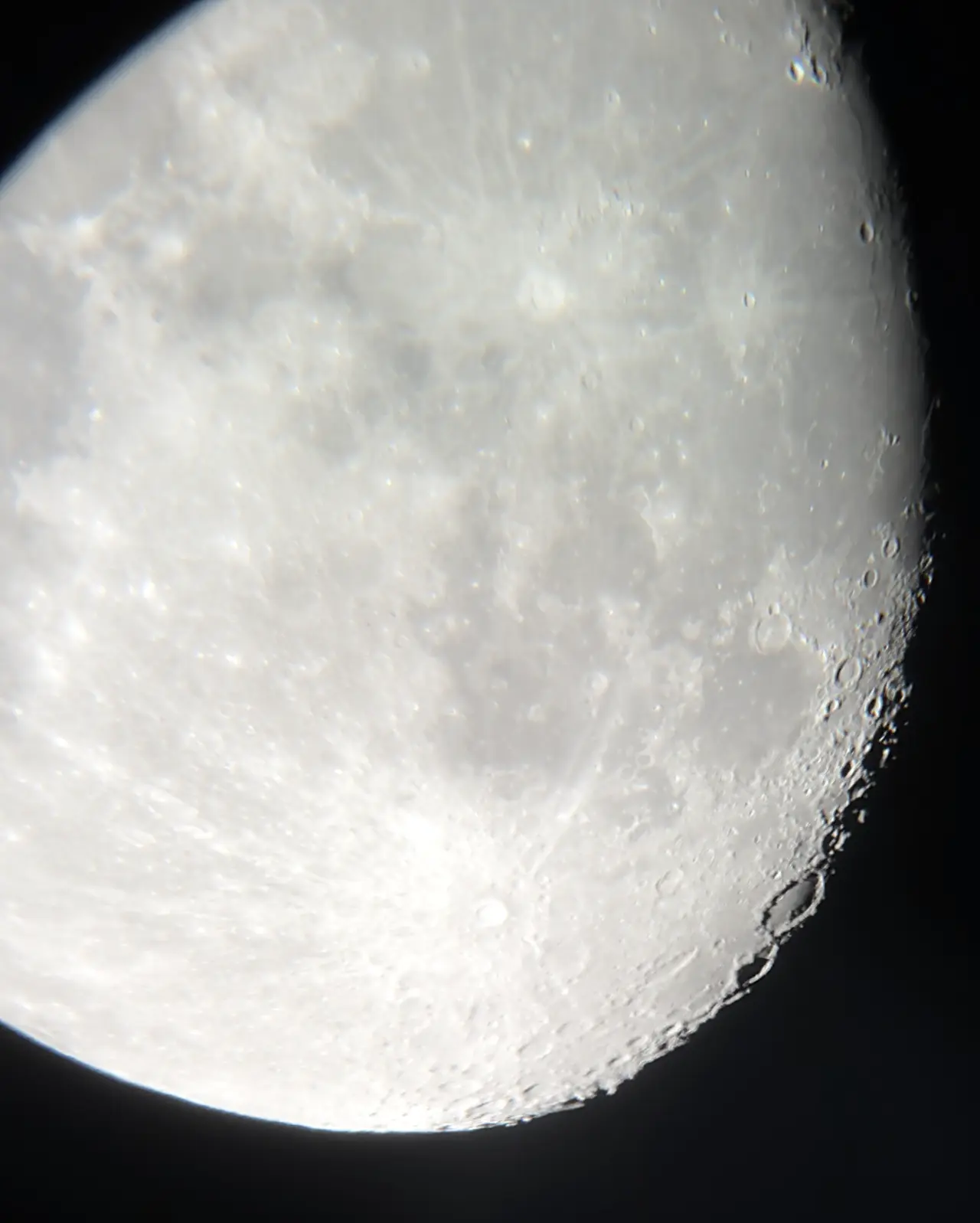 The Moon seen through a telescope eyepiece, a bright gibbous disc with craters sharply shadowed along the terminator