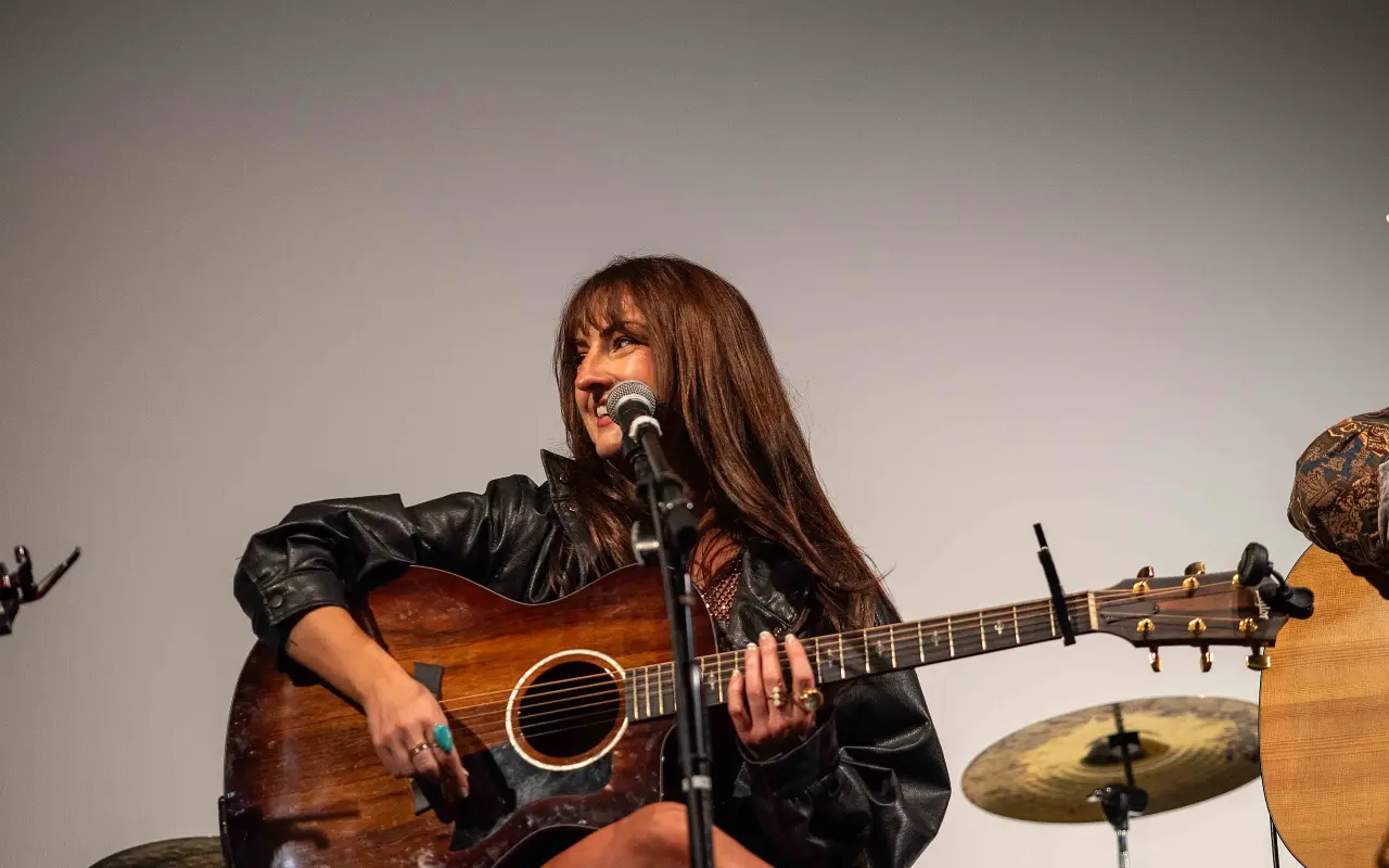 Morgan Johnston seated with an acoustic guitar at a microphone on the Strand stage