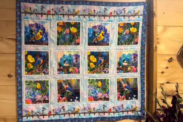 A hand stitched songbird quilt hanging in the Hall