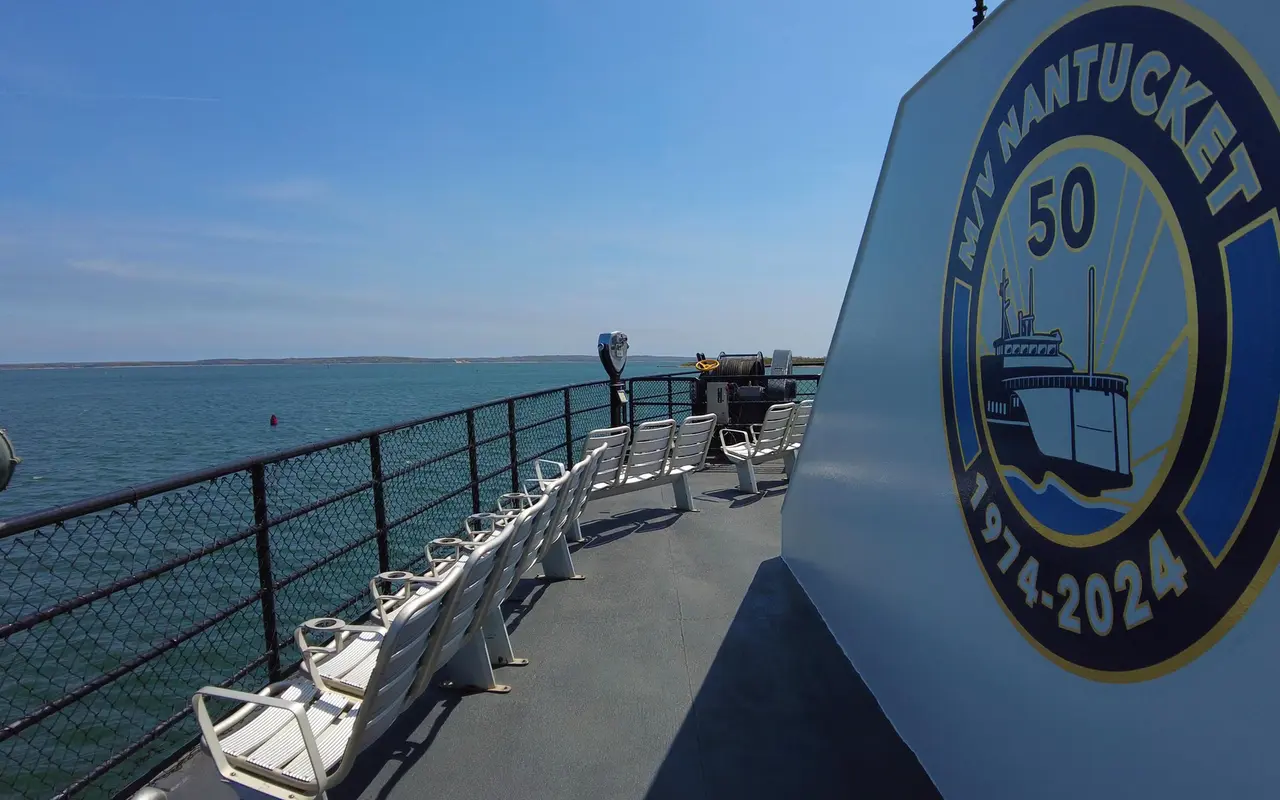 Upper deck of the ferry M/V Nantucket with rows of white seats along the railing and a round 50th anniversary emblem reading 1974-2024 on the cabin wall