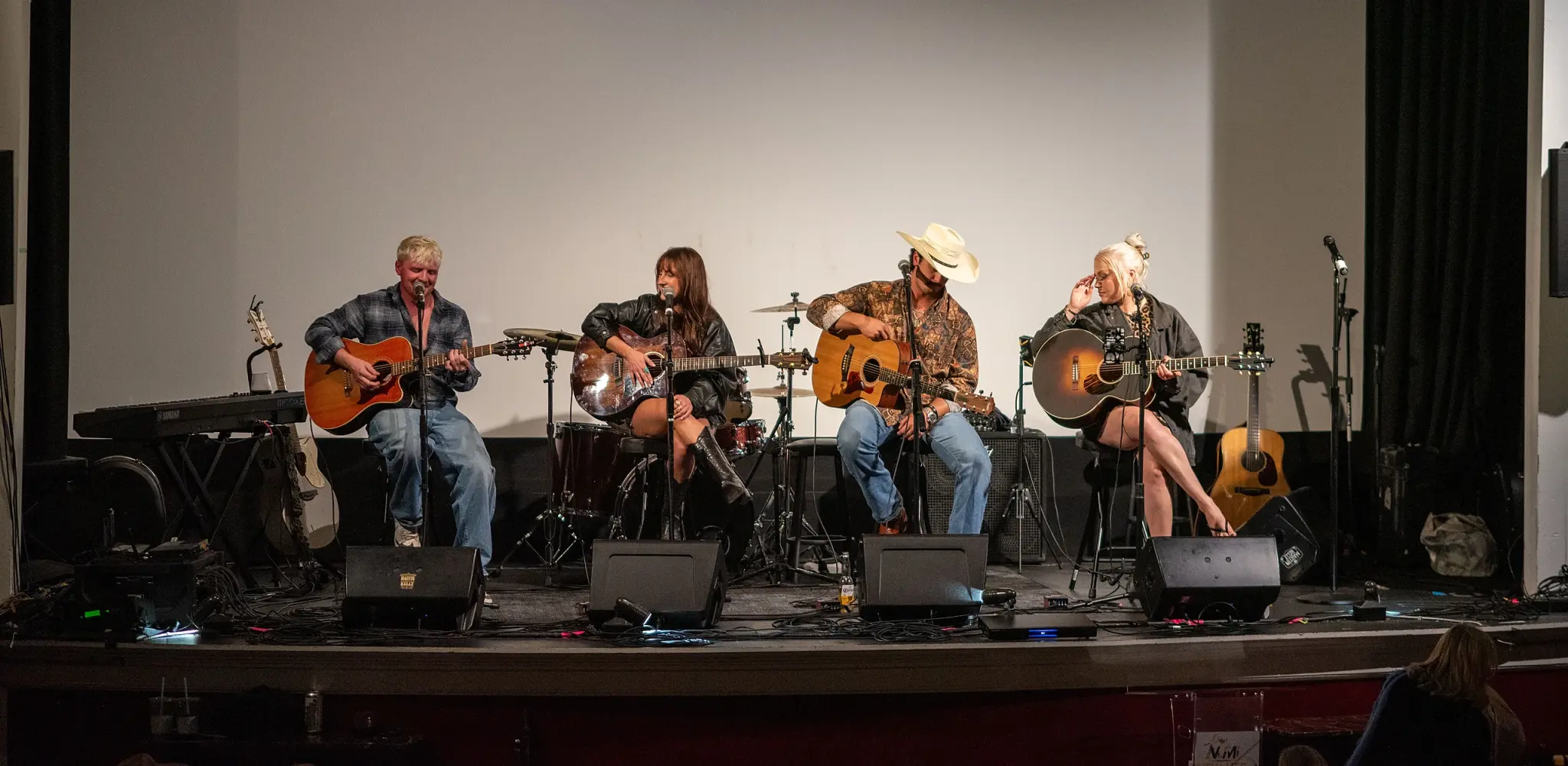 Four songwriters seated with acoustic guitars across the Strand Theatre stage in Oak Bluffs
