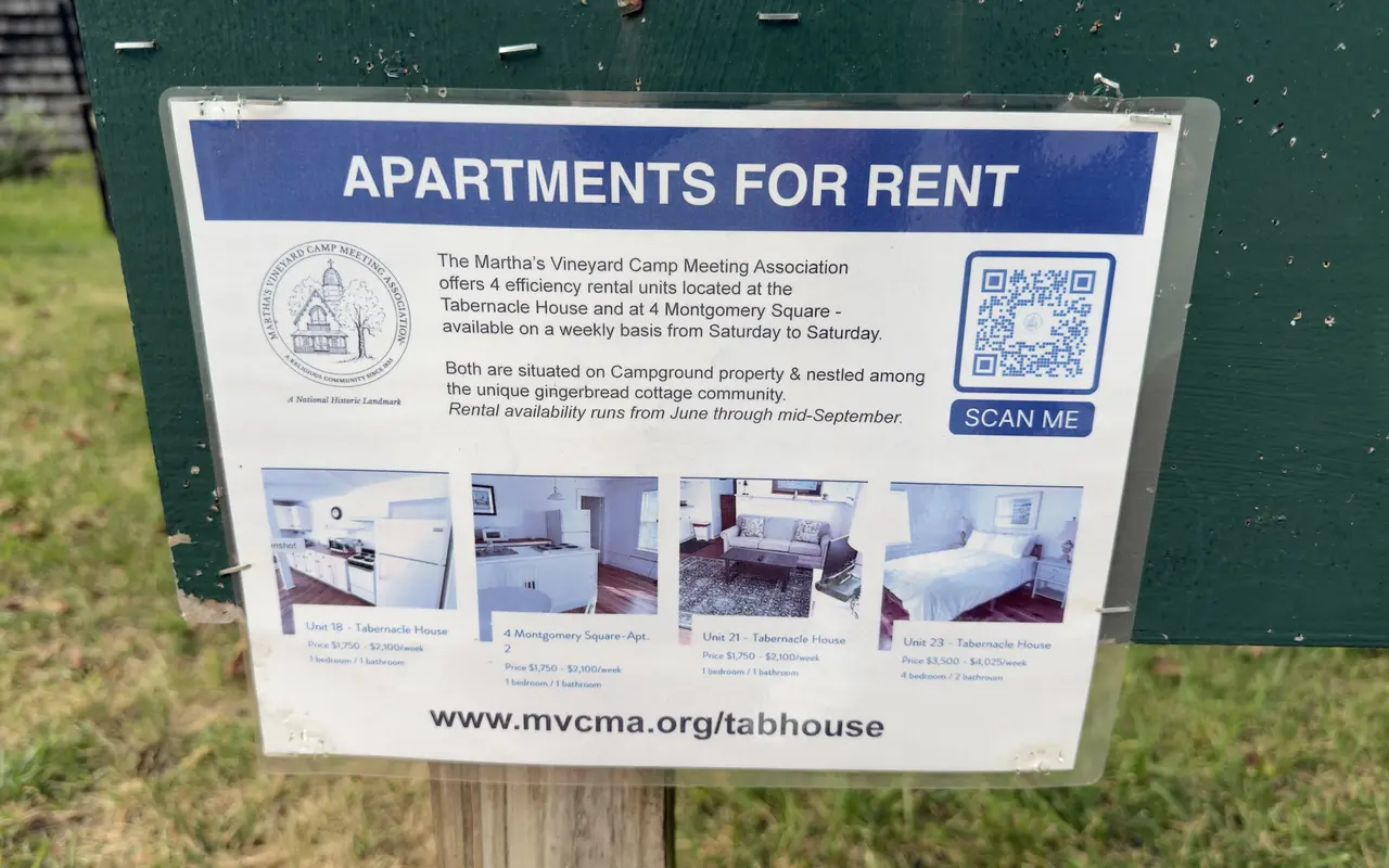 A laminated Apartments for Rent sign on a green notice board: the Martha's Vineyard Camp Meeting Association offers four efficiency rental units at the Tabernacle House and 4 Montgomery Square, weekly Saturday to Saturday, June through mid-September, with photos and weekly prices and the address mvcma.org/tabhouse