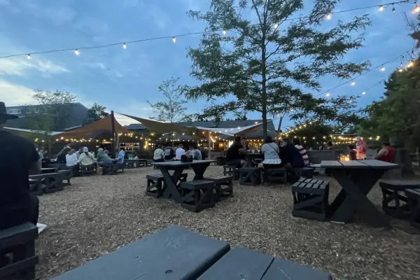 Evening crowd at picnic tables under string lights at Nomans