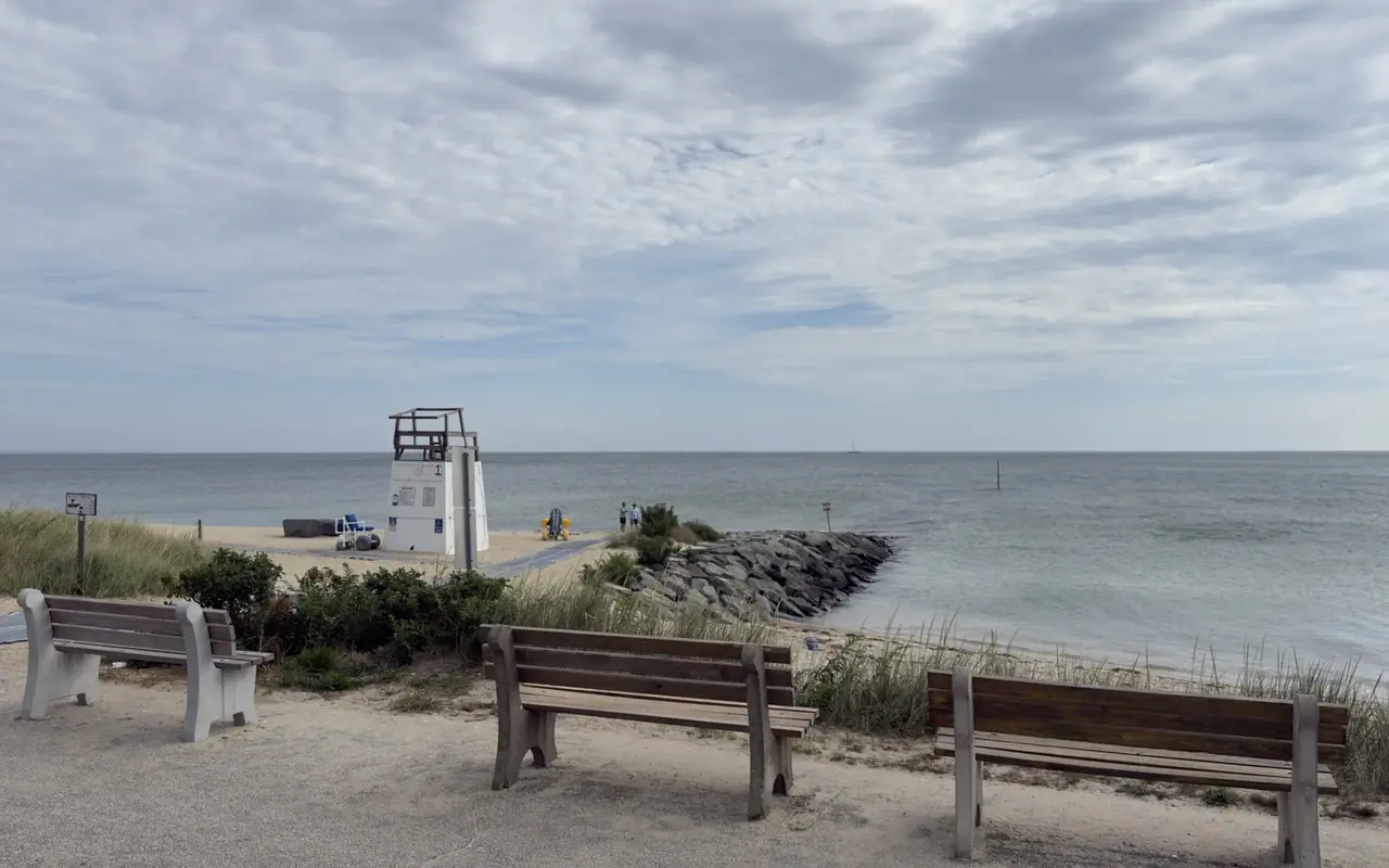 Three wooden benches above an Oak Bluffs beach, with lifeguard stand 1, a mat across the sand, beach wheelchairs and a rock jetty