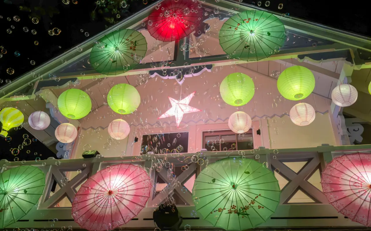 Cottage decorated with parasols and lanterns as bubbles float past on Illumination Night