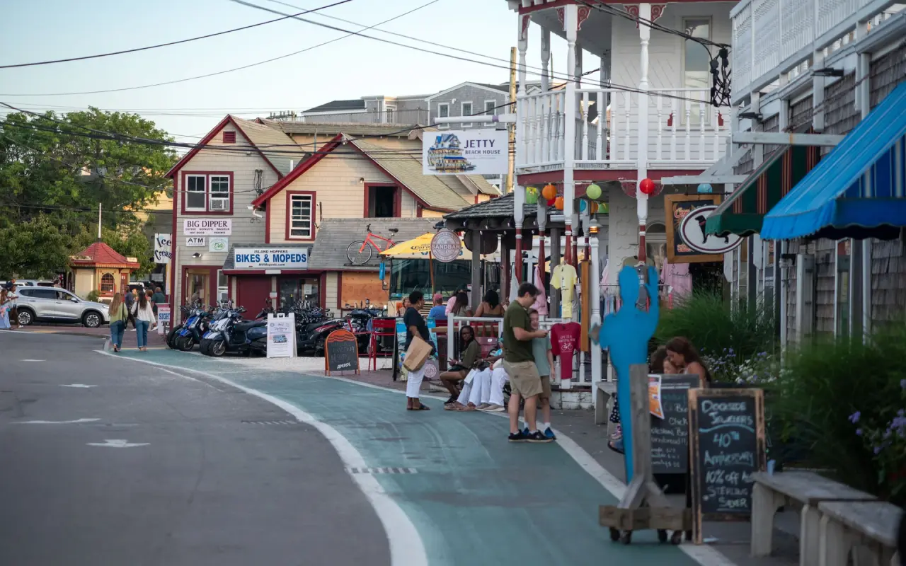 A harborside walkway in Oak Bluffs with shopfronts, flags and people strolling in summer
