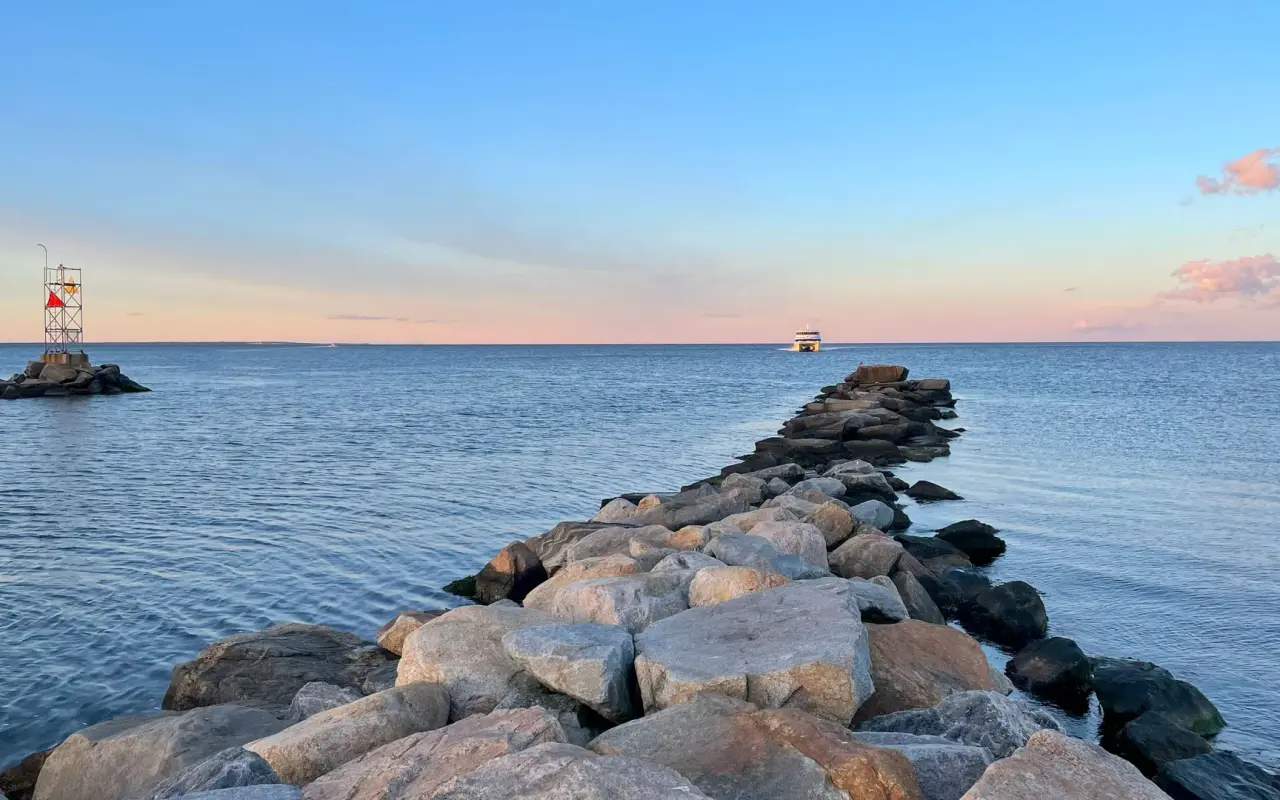 Stone jetty extending into calm water at sunset with a distant boat