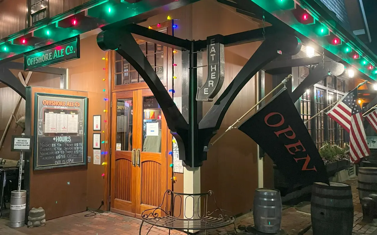 Offshore Ale Co entrance decorated with colored lights and an OPEN flag in winter