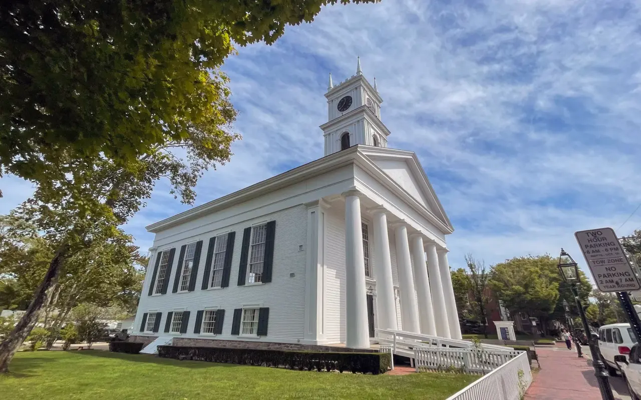 The Old Whaling Church in Edgartown seen from the lawn under a tree, with its columns, clock tower and a white railed ramp along the right side