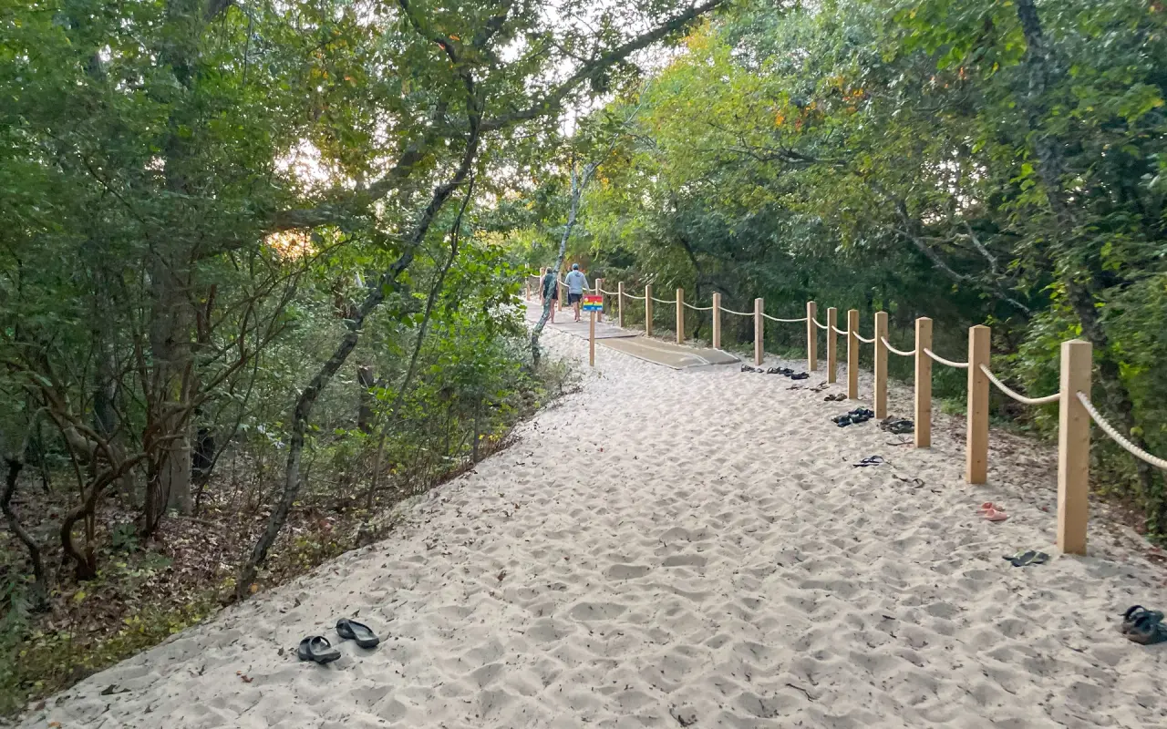 Sandy wooded path with a rope fence leading to Lambert’s Cove Beach