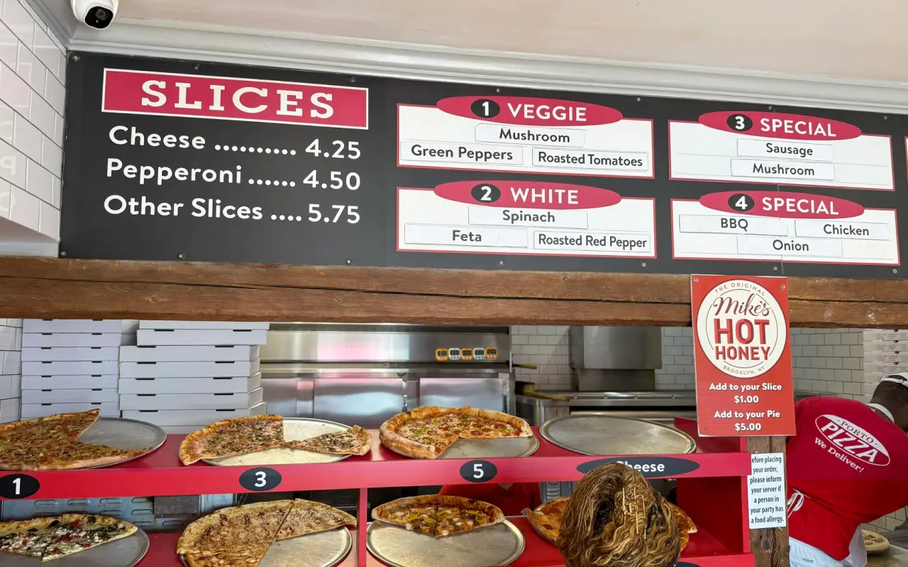 Pizza slices displayed under the menu board at Porto Pizza in Vineyard Haven