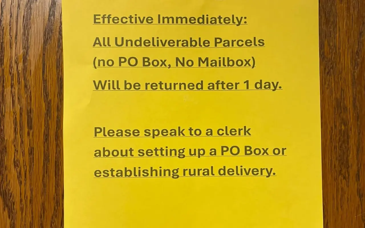 A yellow notice on a post office door: all undeliverable parcels with no PO Box or mailbox will be returned after one day; speak to a clerk about a PO Box or rural delivery