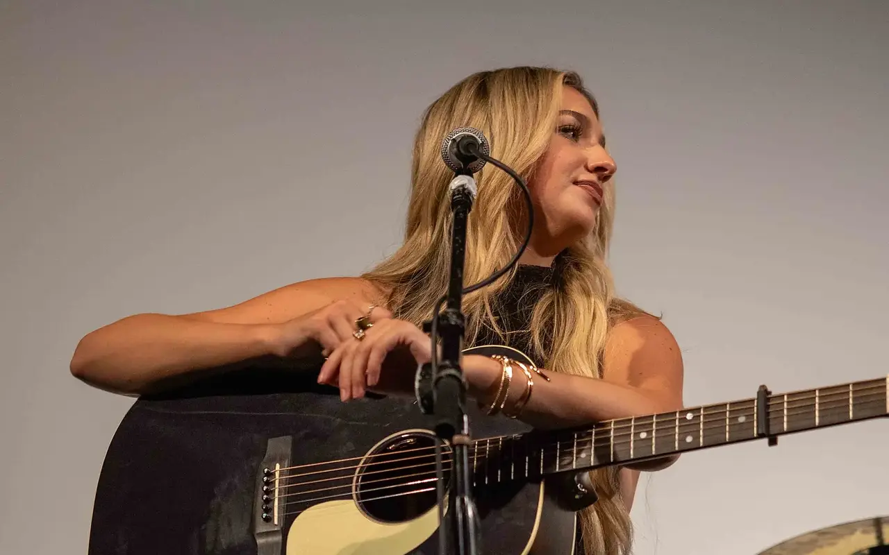 Presley Tennant with her arms folded over a black acoustic guitar, looking to the side