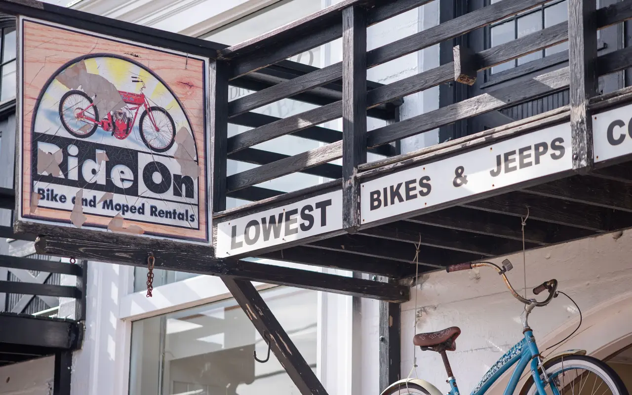 Ride On Bike and Moped Rentals sign on a black balcony with a blue bicycle below