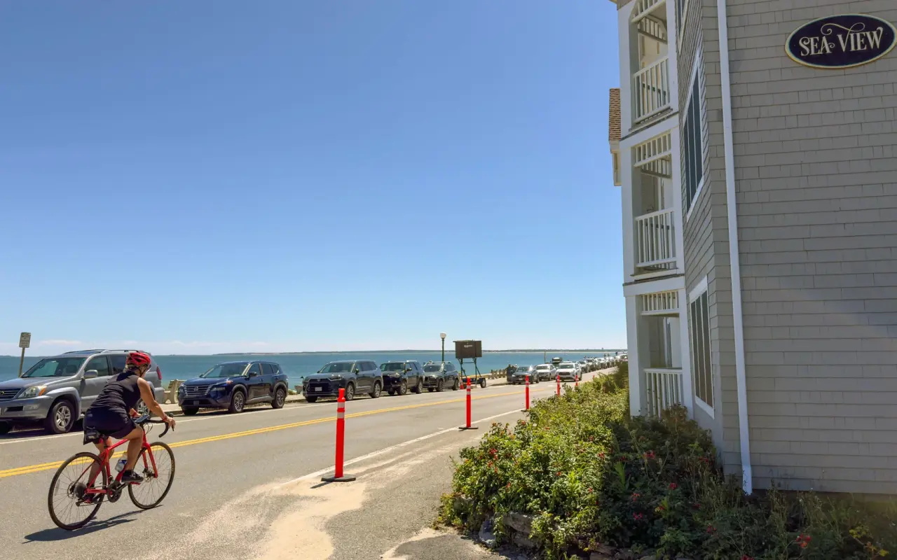 Cyclist riding along Sea View Avenue in Oak Bluffs with parked cars and calm blue water beyond