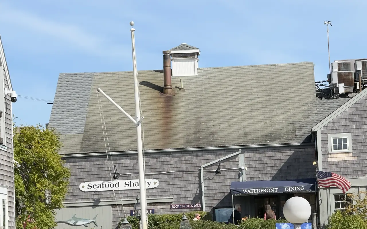 The gray-shingled Seafood Shanty building on Dock Street in Edgartown with its name board, a swordfish carving, a Roof Top Deck Open sign and a navy Waterfront Dining awning