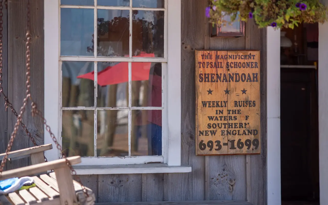 Weathered wooden sign for the topsail schooner Shenandoah beside a window and a porch swing