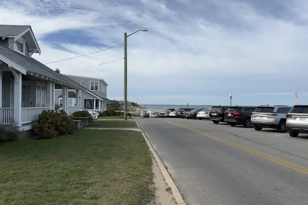 A street of shingled cottages running down to the water in Oak Bluffs, cars angle-parked along it