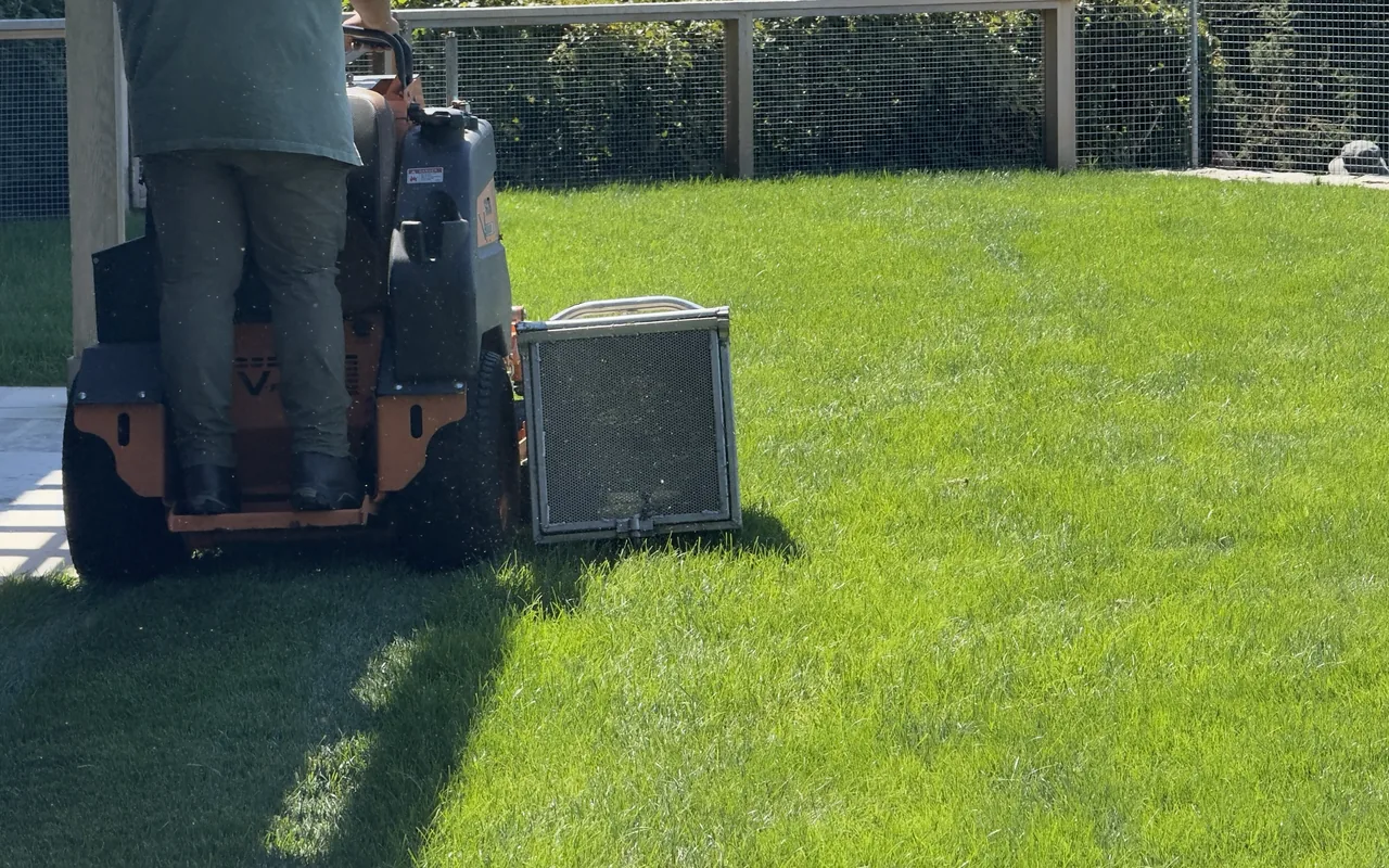 A landscaper on a stand-on mower cutting a fenced lawn on Martha's Vineyard