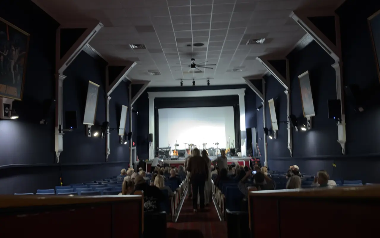 The auditorium of the Strand Theatre in Oak Bluffs filling up before a show: rows of blue seats, framed film posters on the walls and the lit stage under the screen