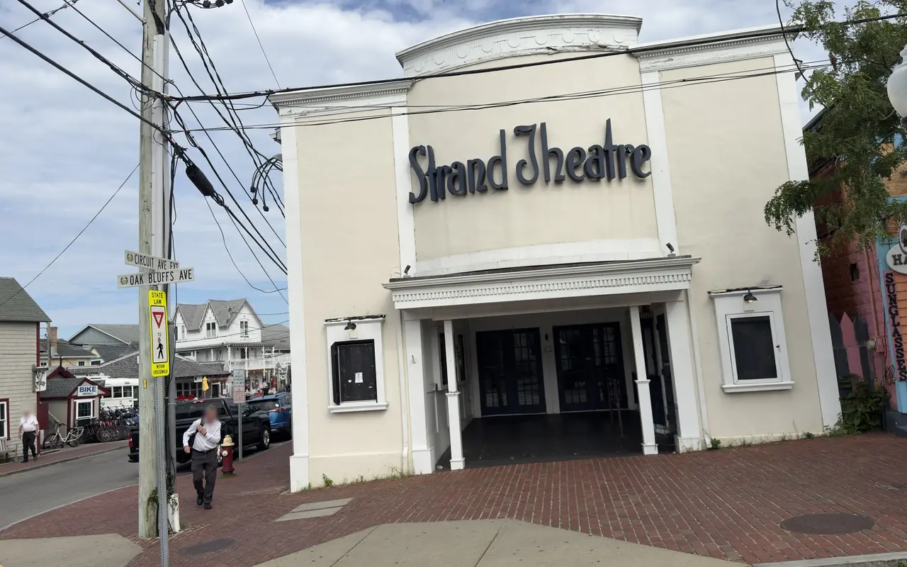 The cream stucco front of the Strand Theatre on Oak Bluffs Avenue, with the Circuit Avenue street sign and gingerbread cottages behind