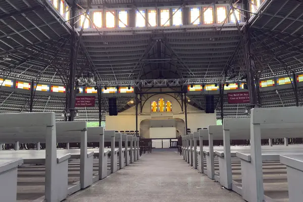 Inside the 1879 Tabernacle on a quiet day: white benches, iron trusses and colored glass along the clerestory