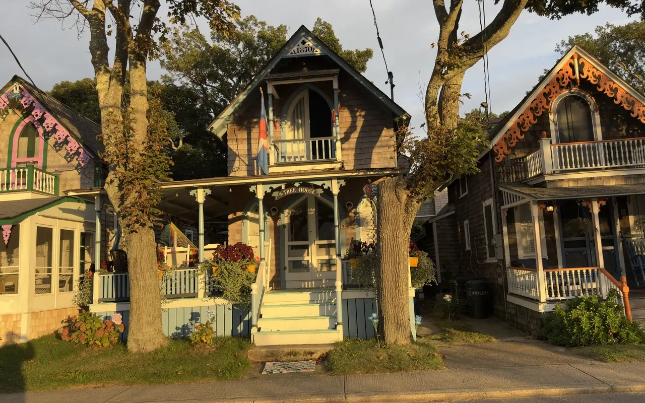 The Tree House, an 1870 cottage in the Oak Bluffs Campground between two oaks, with a pink-trimmed neighbor on the left and an orange-trimmed one on the right