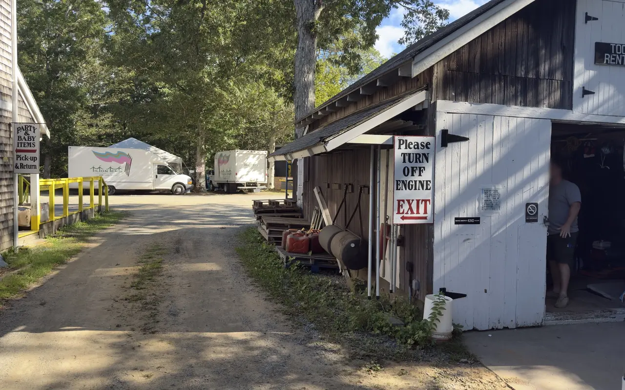 The yard at Tilton Tents and Party Rentals in Vineyard Haven: the tool rental barn with its exit sign, Tilton Tents trucks parked under the trees, and the party and baby items pick-up window