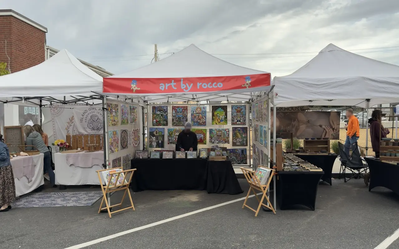 Three vendor tents on Tivoli Day in Oak Bluffs: an Art by Rocco print booth in the middle, a handmade jewelry tent on the left and a pottery tent on the right