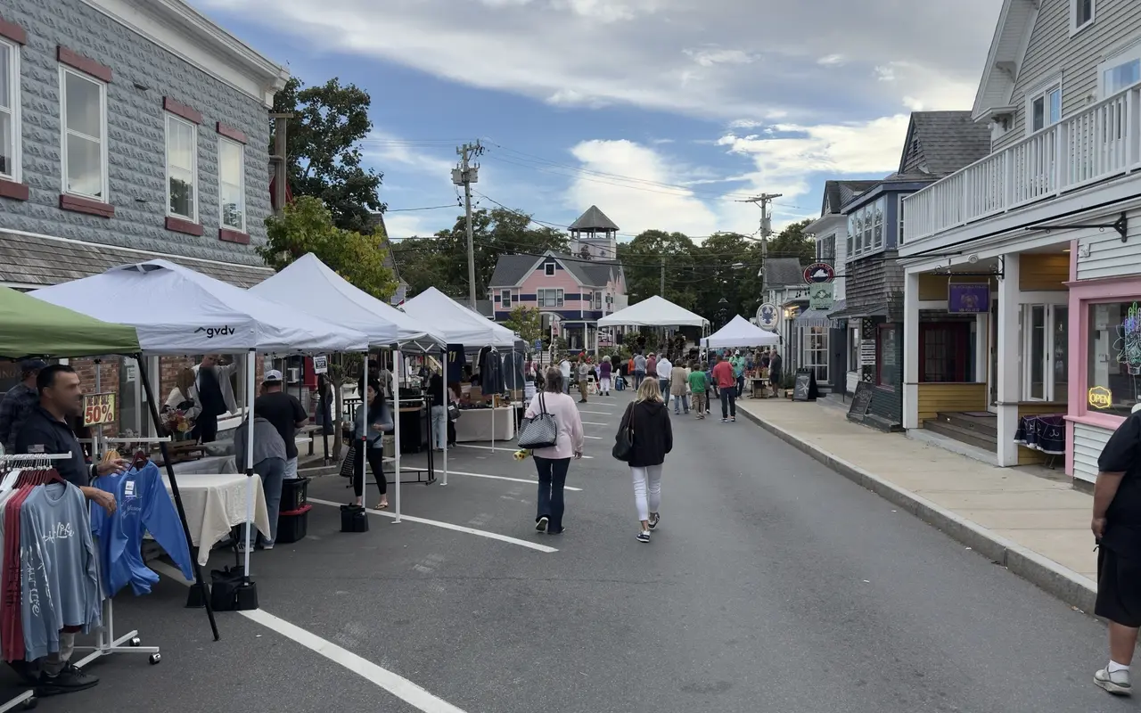 Vendor tents along a closed Circuit Avenue with shoppers walking in the road toward a pink Victorian house