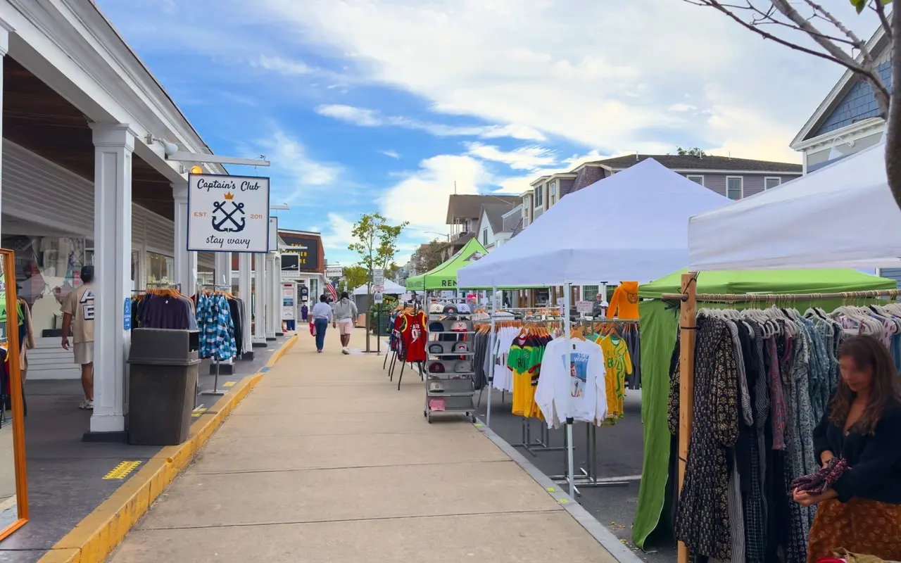 Clothing racks under vendor tents on Circuit Avenue beside the Captain's Club shop sign