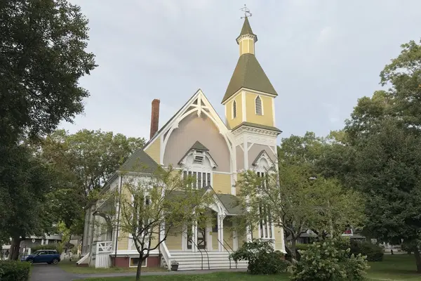 Trinity Methodist Church beside the Tabernacle: yellow clapboard, white Gothic trim and the steeple over the oaks, built 1878
