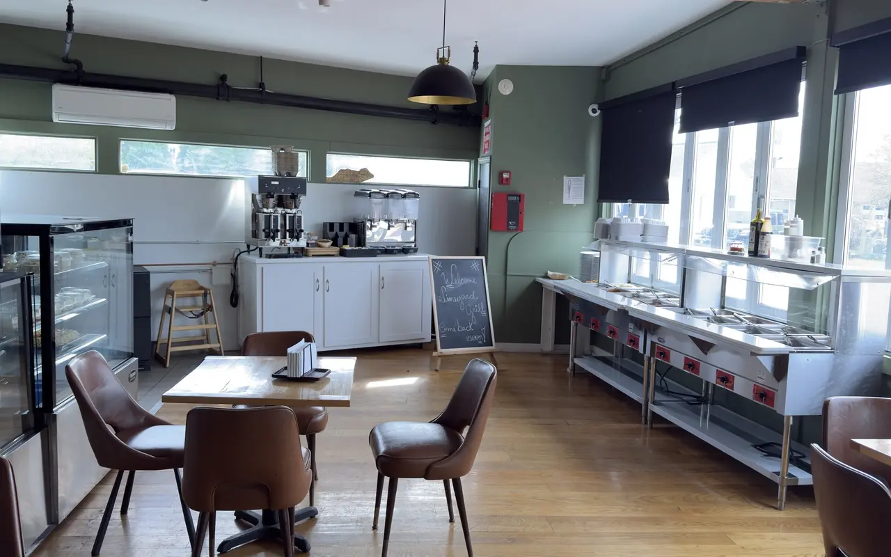 Café room inside the Vineyard Grill in Vineyard Haven with a pastry case, coffee machines, a steam table along the windows and a welcome chalkboard