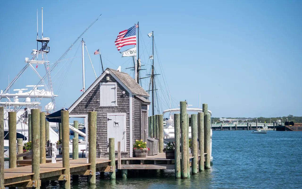 Shingled shed at the end of a wharf with an American flag and boats in the harbor behind
