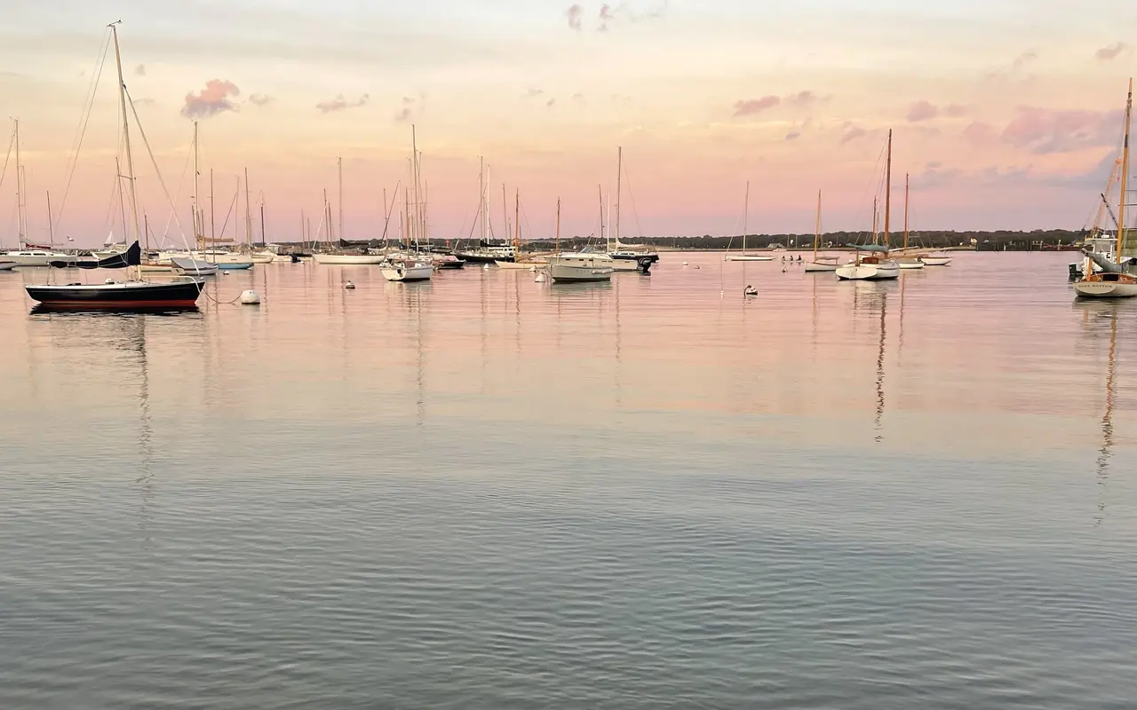 Sailboats and wooden yachts on moorings in Vineyard Haven harbor at dusk, pink clouds reflected in calm water