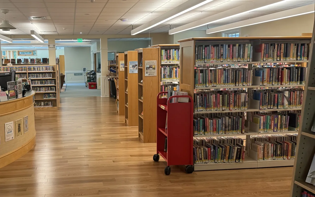 Inside the renovated Vineyard Haven Public Library with oak floors, bookshelves and a red book cart