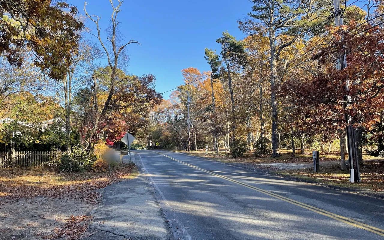 A two-lane road with a double yellow line running between oaks and pines in orange, red and gold autumn color under a blue sky
