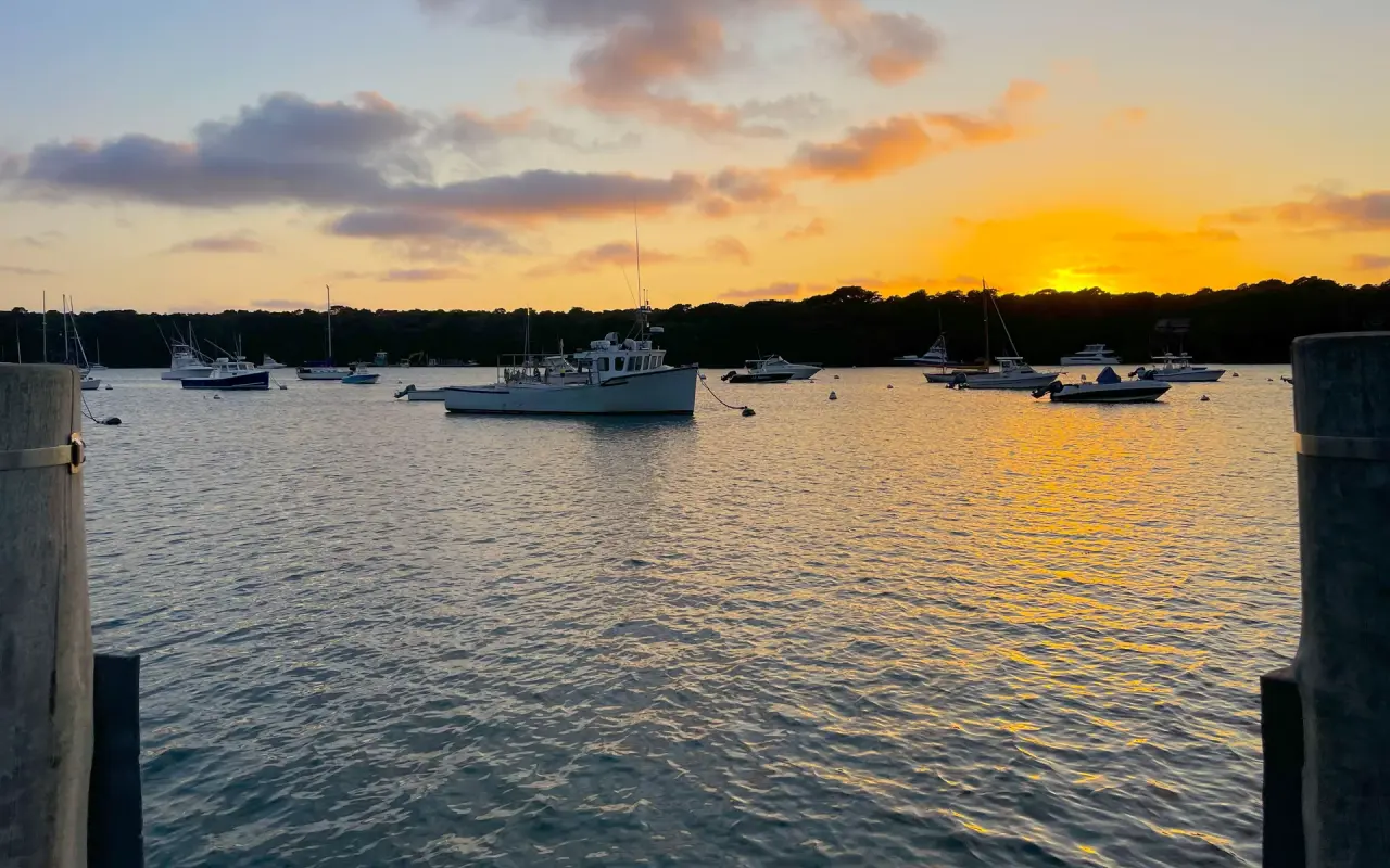 Moored boats on Lake Tashmoo at sunset with an orange sky over the treeline