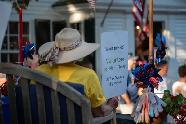 An Oak Bluffs Tree Stewards volunteer holding a "Volunteer to Plant Trees" sign in the Edgartown parade