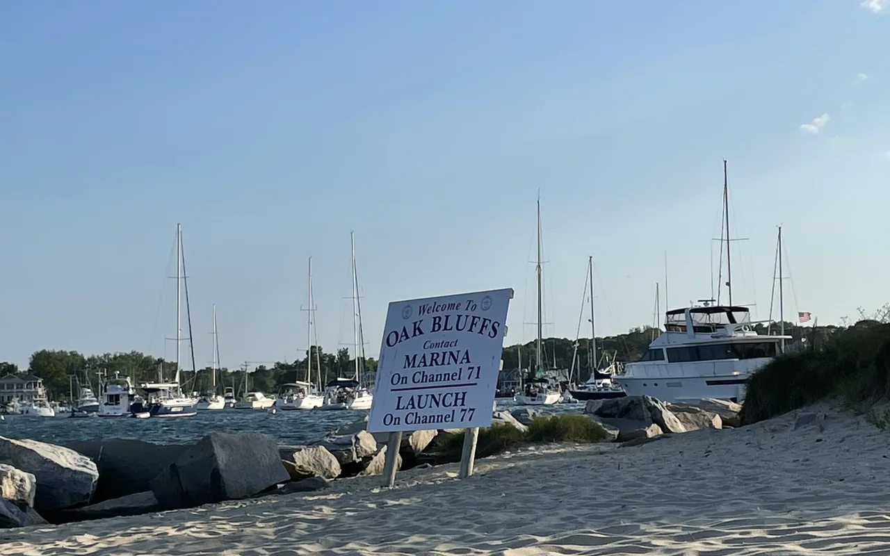 Welcome to Oak Bluffs marina sign on the jetty beach with sailboats in the harbor