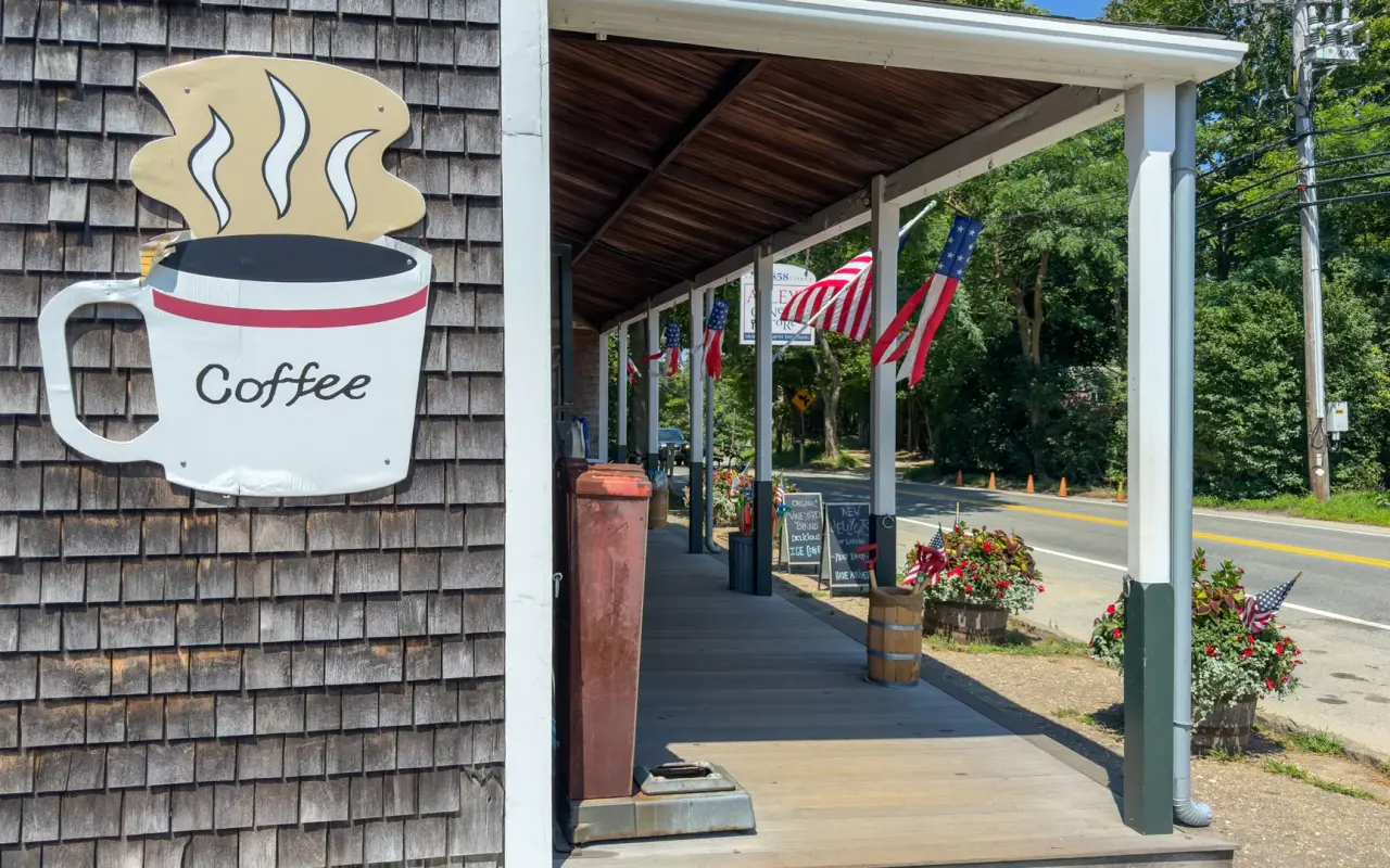 The front porch of Alley's General Store in West Tisbury with a coffee sign, American flags and State Road beyond