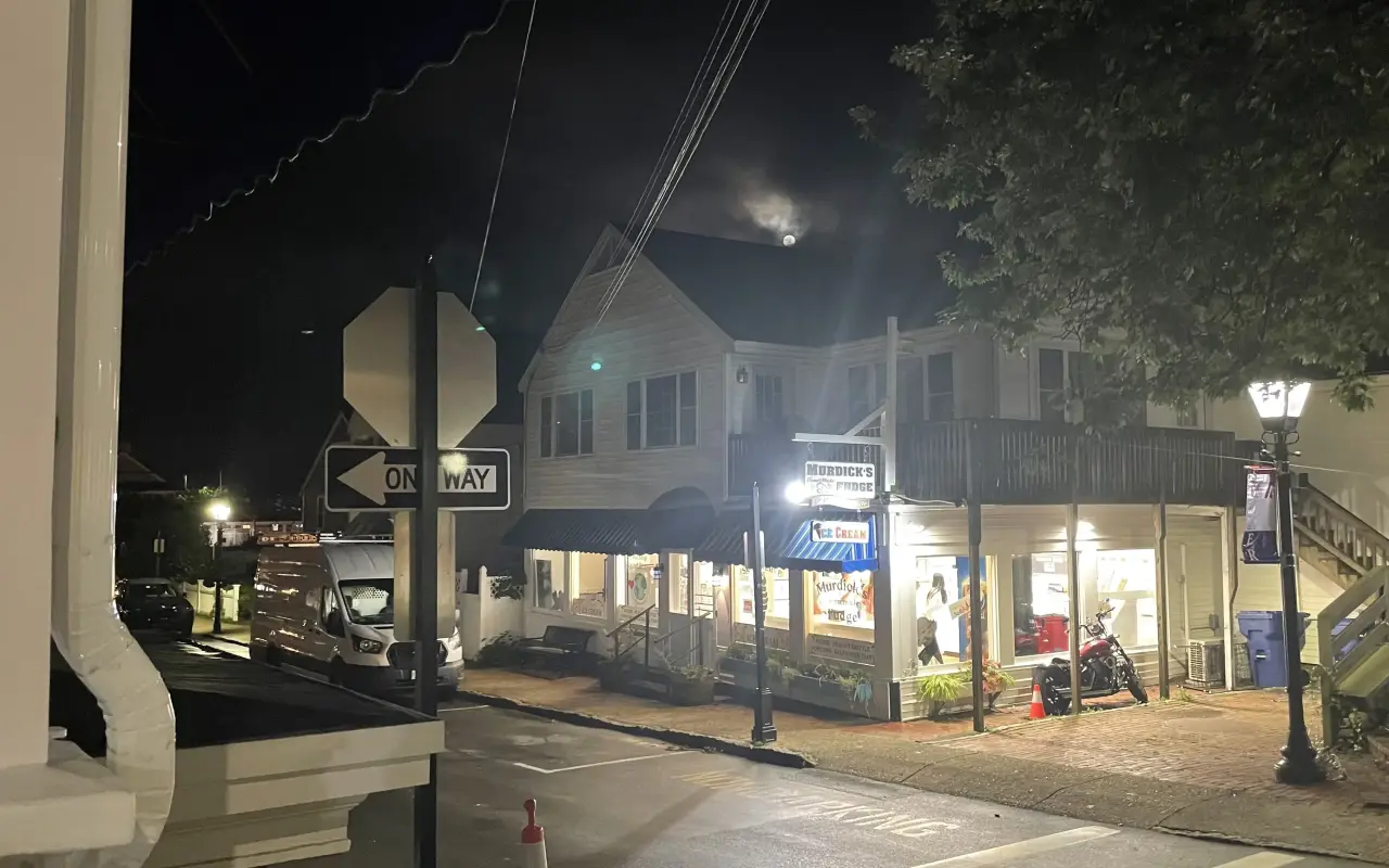 Main Street in Vineyard Haven at night with lit shopfronts and the moon behind a rooftop