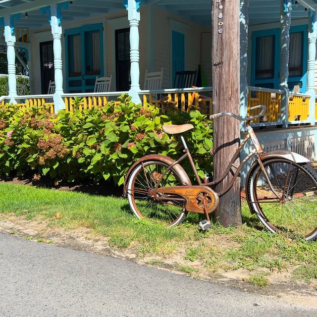 An old Columbia bike leaning against a pole in Oak Bluffs, next to a gingerbread cottage and a row o...